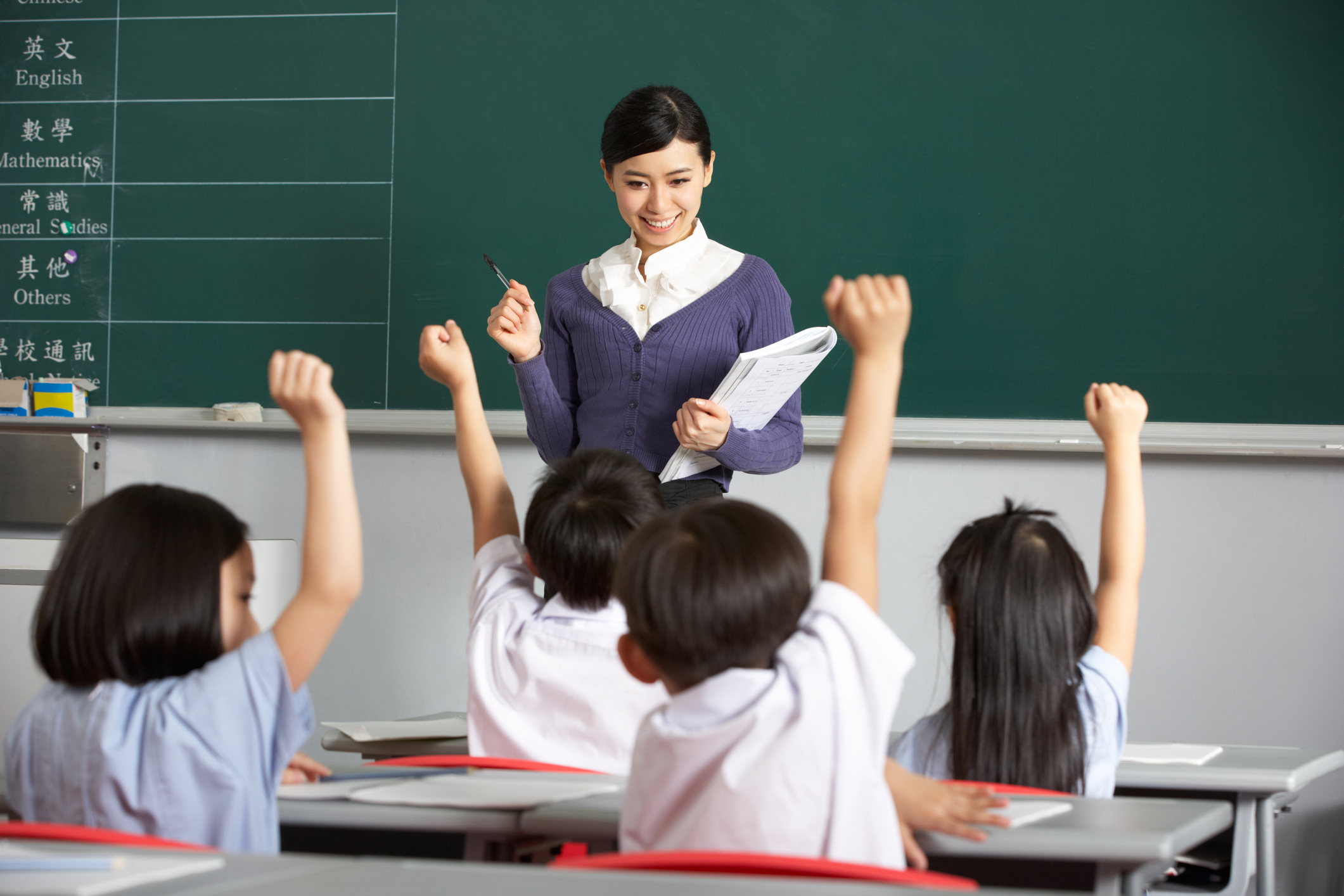 Students In A chinese School Classroom Putting Up Their Hands To Answer The Teacher